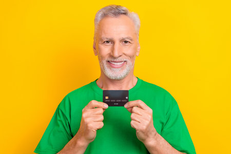 Photo of positive good mood guy dressed green t-shirt rising showing bank card isolated yellow color...