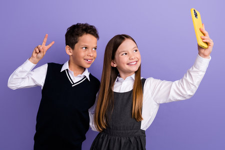 Photo of positive friends schoolkids make selfie on smart cell gadget with v sign isolated purple...