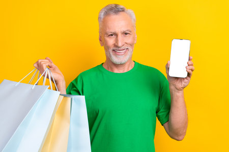 Photo of cheerful positive guy dressed green t-shirt holding modern device empty space online shopping isolated yellow color backgroundの写真素材