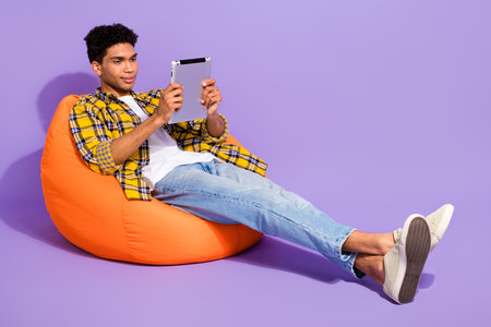 Full size photo of positive nice person sit comfort bag use tablet chatting social network isolated on violet color backgroundの写真素材