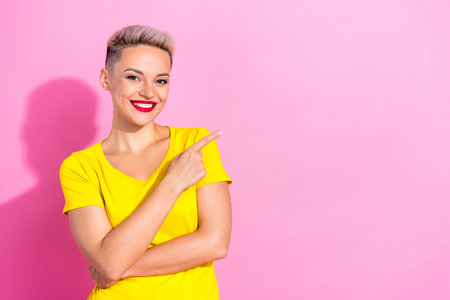 Portrait of pretty cheerful girl indicate finger empty space proposition isolated on pink color backgroundの写真素材