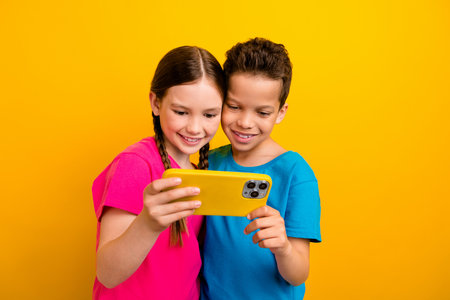 Photo of sweet adorable preteen schoolchildren wear t-shirts watching video modern device isolated...
