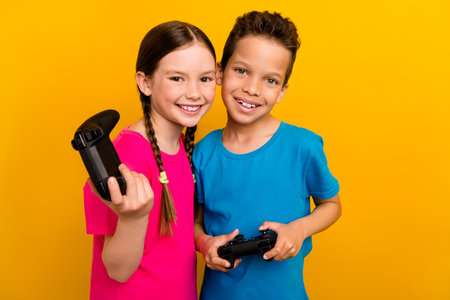 Photo of excited sweet preteen schoolchildren wear t-shirts enjoying game isolated yellow color...