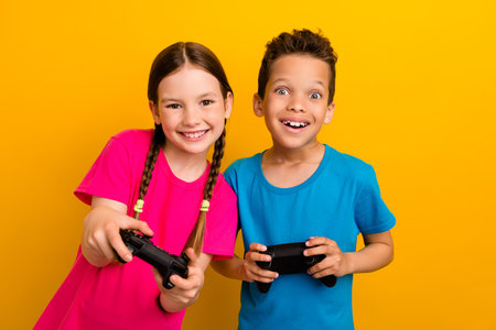 Photo of adorable excited preteen schoolchildren wear t-shirts enjoying game isolated yellow color backgroundの写真素材
