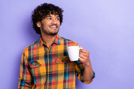 Photo of dreaming young man curls holding cup fresh cappuccino looking empty space coffee break relax isolated over violet color backgroundの写真素材