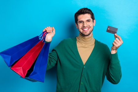 Photo of lucky shopaholic man brunet hair wear trendy cardigan holding plastic credit card buy things isolated on blue color backgroundの写真素材