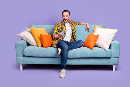 Photo of confident man boss wear plaid trendy clothes rest sit soft couch divan writing sms read news isolated on purple color backgroundの写真素材