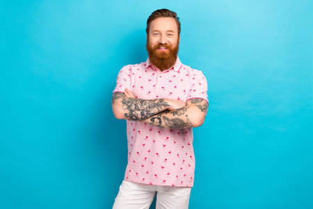 Portrait of optimistic friendly man with cool tattoo wear flamingo t-shirt standing hold arms crossed isolated on blue color backgroundの写真素材