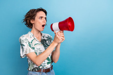 Portrait of gorgeous woman with stylish hairdo wear print shirt look empty space scream in loudspeaker isolated on blue color backgroundの写真素材