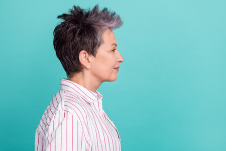 Profile portrait of charming pensioner woman looking empty space fashionable haircut isolated teal color backgroundの写真素材