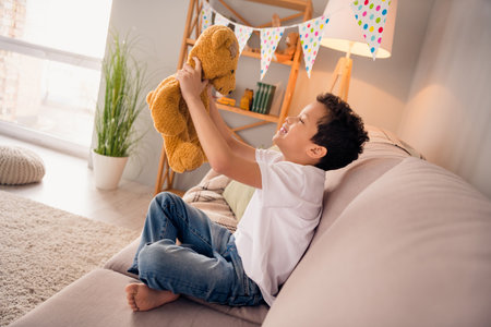 Photo of joyful cute kid boy holding soft fluffy teddy bear parents birthday present favorite toy in nursery roomの写真素材
