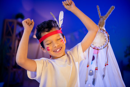 Photo of positive kid in native american costume enjoy preschool theme halloween party dance raise fist up indoorsの写真素材