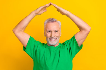 Photo of cheerful positive guy dressed green t-shirt showing arms roof isolated yellow color...