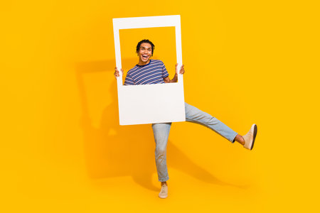 Full body photo of overjoyed carefree person dancing hold paper album card window isolated on yellow color backgroundの写真素材
