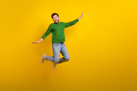 Full size cadre of crazy flying jumping shopaholic guy wearing denim jeans stylish outfit wings arms isolated on yellow color backgroundの写真素材