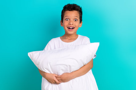 Photo of cheerful astonished little boy open mouth arms hold comfy pillow cushion isolated on teal color backgroundの写真素材
