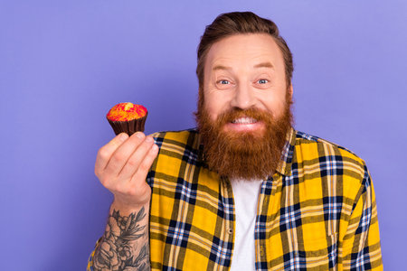 Photo of glad cheerful happy man wear stylish plaid clothes hand hold advertise delicious cupcake isolated on purple color backgroundの写真素材