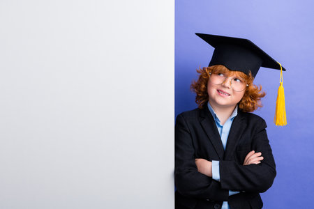 Portrait of little minded schoolchild crossed arms wear mortarboard hat look empty space banner isolated on purple color backgroundの写真素材