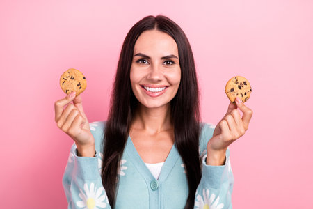 Photo of cheerful positive lady wear flower print cardigan holding two chocolate biscuits isolated pink color backgroundの写真素材