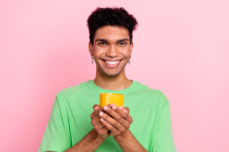 Photo of attractive cute guy wear green t-shirt smiling enjoying coffee isolated pink color backgroundの写真素材