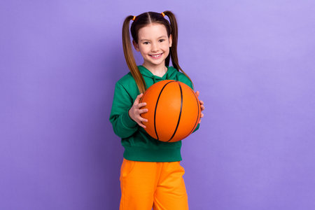 Photo of cheerful positive small girl wear green sweatshirt playing basketball isolated violet color backgroundの写真素材