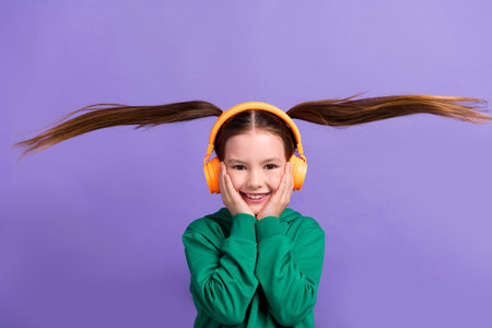 Photo of impressed cute small girl wear green sweatshirt arms cheeks listening songs flying tails...