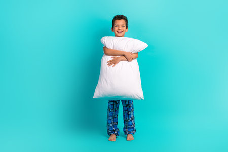Full body portrait of excited cheerful schoolkid have good mood arms hold big cushion isolated on turquoise color backgroundの写真素材