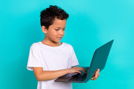 Portrait of positive lovely schoolchild use wireless netbook typing chatting isolated on turquoise color backgroundの写真素材