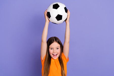 Photo of funny energetic football support young girl raise hands with sport equipment win tournament isolated on purple color backgroundの写真素材