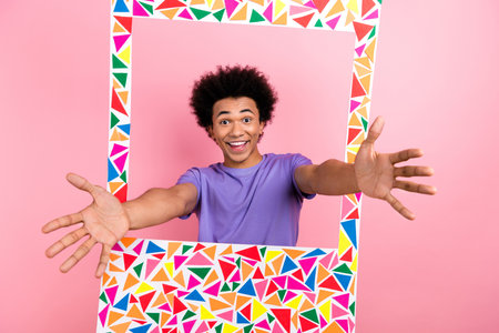 Photo of overjoyed cheerful man wear purple clothes peek out hole open arms glad see you isolated on...