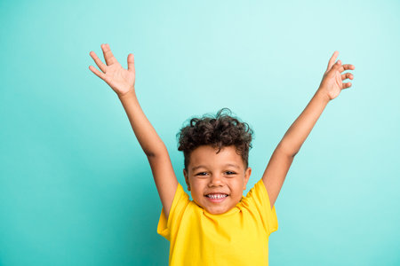 Photo of satisfied friendly schoolboy with brown hair dressed yellow t-shirt raising palms up...