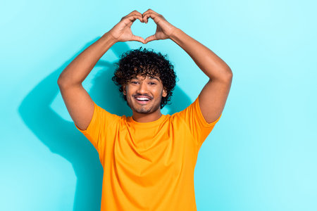Photo of friendly cheerful person toothy smile arms fingers demonstrate heart symbol above head isolated on teal color backgroundの写真素材