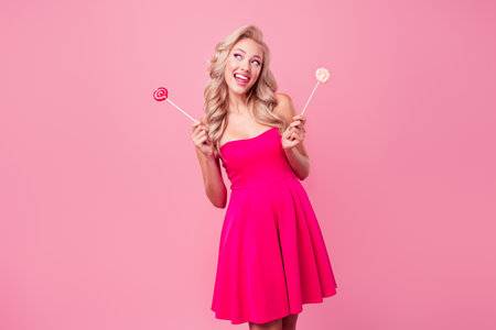 Portrait of cheerful cute minded lady hands hold candy stick lollypop look empty space isolated on pink color backgroundの写真素材