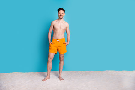 Full body photo of handsome young guy stand sand pockets wear trendy yellow shorts isolated on blue color background summer vacationの写真素材