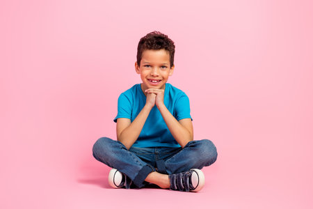 Full length photo of dreamy sweet little boy dressed blue t-shirt sitting floor hands chin isolated...