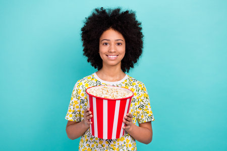 Photo of cute cheerful girl wear trendy clothes hands hold basket delicious pop corn isolated on cyan color backgroundの写真素材
