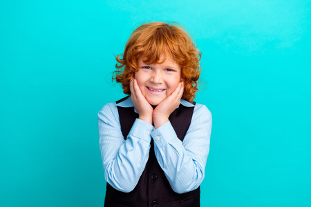 Portrait of adorable friendly schoolkid beaming smile hands touch cheekbones isolated on turquoise...