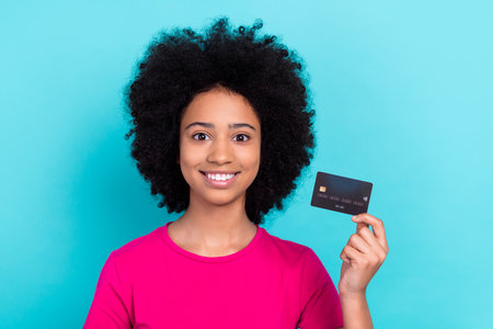 Photo of toothy beaming girl with afro chevelure wear pink t-shirt fingers demonstrate credit card...