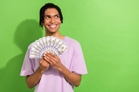 Photo of creative handsome person toothy smile hold dollar bills look empty space isolated on green color backgroundの写真素材