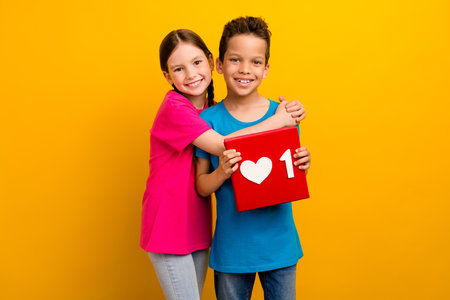 Photo of adorable sweet preteen schoolkids dressed t-shirts hugging holding heart like sign isolated yellow color backgroundの写真素材