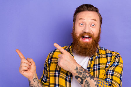 Photo of attractive funny guy indicating fingers empty space overjoyed open mouth isolated purple color backgroundの写真素材