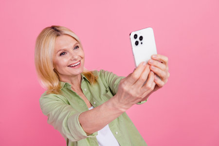 Portrait of positive pretty person beaming smile good mood hold smart phone make selfie isolated on pink color backgroundの写真素材