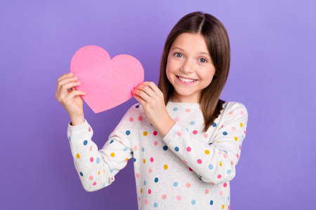 Photo of cheerful positive small girl wear dotted sweater rising pink heart isolated violet color backgroundの写真素材