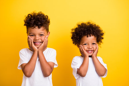 Photo of adorable funky cheerful kids toothy smile hands touch cheeks isolated on vivid yellow color backgroundの写真素材