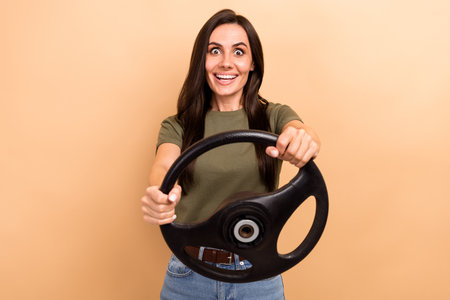 Photo of pretty impressed lady wear khaki t-shirt driving automobile isolated beige color backgroundの写真素材