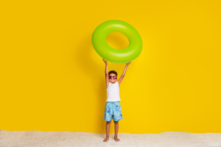 Full length photo of excited funky small boy wear white shirt dark eyewear rising floating circle isolated yellow color backgroundの写真素材