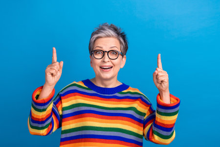 Portrait of astonished cheerful person direct fingers up empty space proposition isolated on blue...