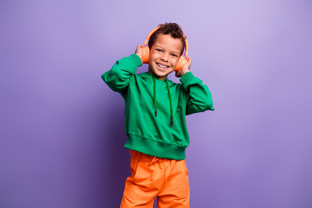 Photo of funky carefree small boy wear green sweatshirt enjoying music headphones isolated violet color backgroundの写真素材