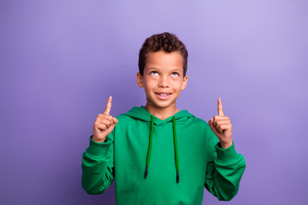 Photo of dreamy thoughtful small boy wear green sweatshirt looking pointing two fingers up empty space isolated violet color backgroundの写真素材