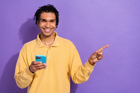 Photo of positive person with dreadlocks wear stylish shirt hold smartphone directing empty space isolated on purple color backgroundの写真素材